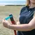 Person demonstrating the use of a dog waste bag dispenser with blue bag, attached to a red handle.