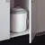 White cat litter container with grey lid, cat face embossing, placed in a cupboard.