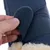 Gros plan sur une main ouvrant une fermeture à scratch sur une botte bleue en tissu avec doublure intérieure en fourrure synthétique beige visible.
