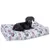 Chien noir et marron allongé sur un grand coussin rectangulaire à motifs colorés (valises, trains, lettres, logos Platform 9 3/4). Housse en tissu imprimé visible.