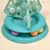 Jouet interactif pour chat en plastique turquoise, forme d’arbre avec balles colorées et motifs découpés (étoiles, sapins) visibles sur la structure.