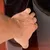 Mano de una persona levantando una tapa o panel negro brillante, posiblemente de plástico o vidrio, sobre una superficie marrón. No se observan marcas ni texto visible.