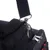 Gros plan sur une sangle en tissu noir avec mousqueton métallique fixée à un sac noir, deux fermetures éclair visibles sur le dessus du sac.