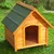 Wooden dog kennel with pitched green shingle roof and open doorway, shown outdoors on grass. No visible brand or text.