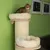 Котка върху бежово легло на високо дървено и въжено котешко дърво с две меки легла, разположени едно над друго, пред зелена стена.