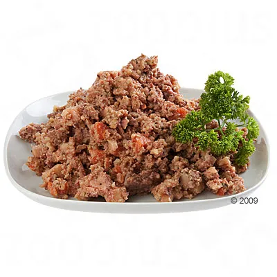 Порция смляна консервирана храна за домашни любимци, сервирана в бяла чиния с клонка магданоз отстрани. Видими парчета месо и зеленчуци.