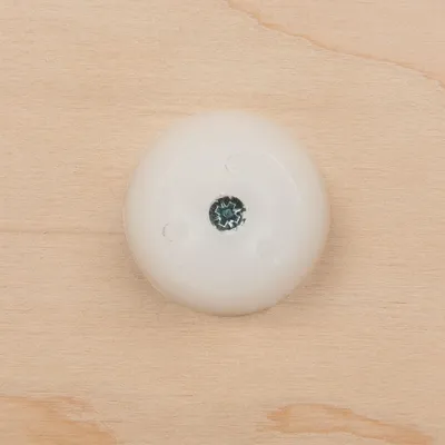 Disco rotondo in plastica bianca fissato con una vite su superficie in legno chiaro, senza marchi o testo visibili.
