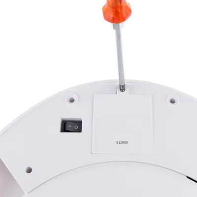Instructie voor het openen van het batterijvak met een schroevendraaier op een wit apparaat. Zichtbaar: aan/uit-schakelaar en CE-markering.