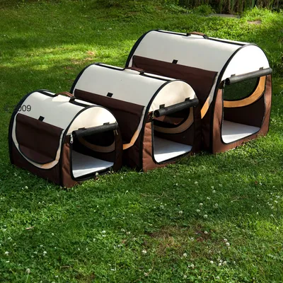 Trois caisses de transport pour animaux en tissu marron et beige, tailles petite, moyenne et grande, avec ouvertures zippées et fenêtres en maille visibles sur l’herbe.