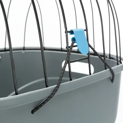 Détail d’une cage en métal noir et plastique gris avec attache bleue et corde noire visible sur le côté supérieur.