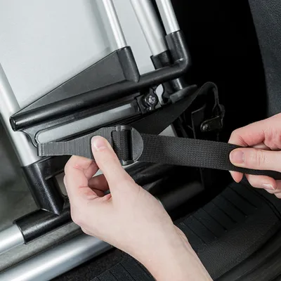 Hand befestigt einen Sicherheitsgurt an einer Transportbox mit Metallrahmen. Anleitung zur sicheren Fixierung der Box im Fahrzeug.