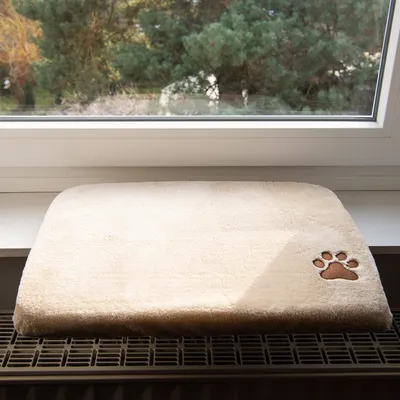 Beige windowsill mat made of soft fabric with embroidered brown paw print appliqué, placed on a radiator cover.