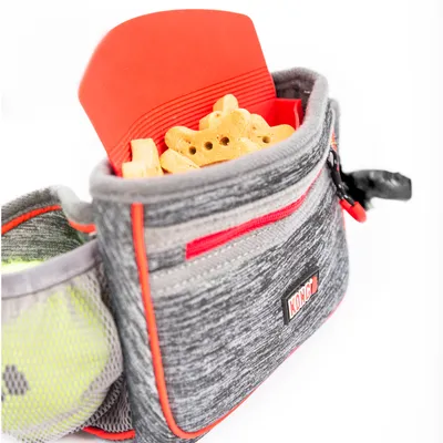 KONG borsa porta-snack in tessuto grigio con cerniera rossa, riempita con biscotti per cani. Tasca laterale in rete visibile.