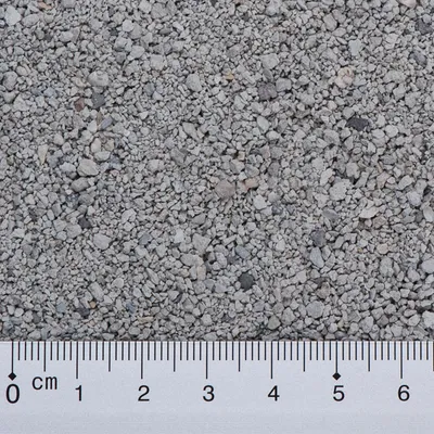 Vista de grava o arena gruesa gris con regla en centímetros mostrando el tamaño de los granos, que varían entre 0 y 5 cm.