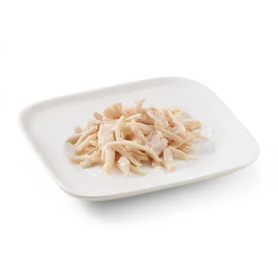 Close-up of tender, white chicken meat strips on a white plate, served in natural juice.