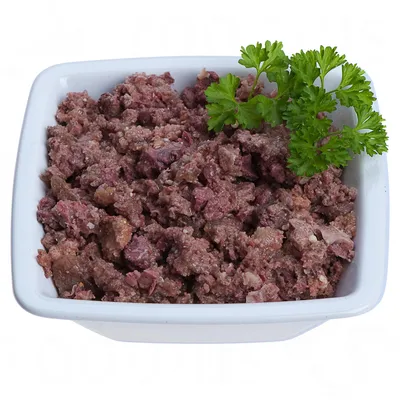 Lähikuva raasta, pilkotusta lihasta valkoisessa kulhossa, koristeltu tuoreella persiljalla.