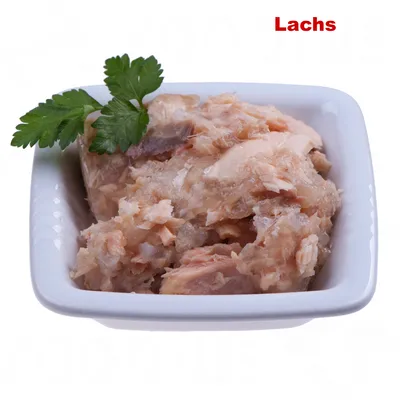Nahaufnahme von zerkleinertem Lachs in einer weissen Schale, dekoriert mit einem frischen Petersilienzweig. Text 'Lachs' oben rechts sichtbar.