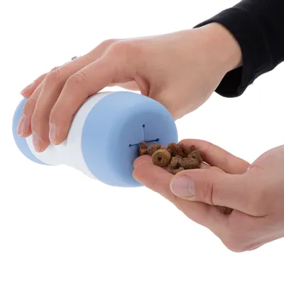 Hand zeigt die Verwendung eines blauen Futterspenders, der Trockenfutter in die Hand ausgibt.
