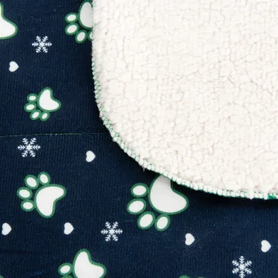 Nahaufnahme einer Decke mit weißer, flauschiger Oberfläche und dunkelblauem Stoff mit grünen Pfotenabdrücken und Schneeflocken-Motiven.
