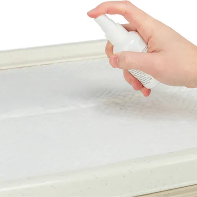 Hand sprays liquid from a white spray bottle onto an absorbent pad.