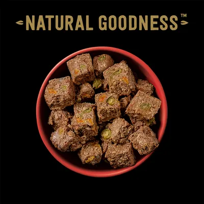 Natural Goodness -merkkisiä kuutioituja lemmikkiruokapaloja punaisessa kulhossa, näkyvissä vihreitä ja oransseja ainesosia paloissa.