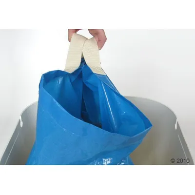 Blå plastpose med beige stofhåndtag, holdt af en hånd. Posen er placeret i en grå beholder. Materialer: plast og stof.