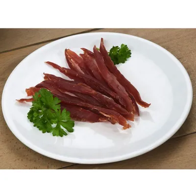 Ленти сушено месо, подредени върху бяла чиния с две стръкчета магданоз. Видимият материал е месо.