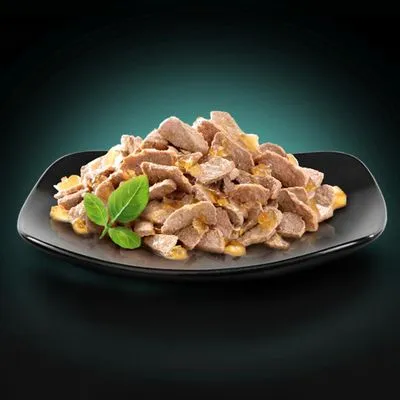 Portie natvoer met stukjes vlees in saus, geserveerd op een zwart bord met basilicumblaadjes. Geen merknaam of verpakking zichtbaar.