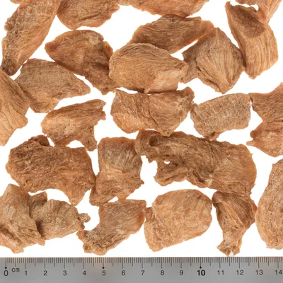 Morceaux de friandises brunes déshydratées pour animaux, disposés sur fond blanc avec une règle en centimètres indiquant la taille des morceaux, environ 3 à 6 cm chacun.