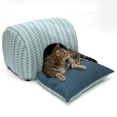 Kattehule med blåt zigzag-mønster og matchende pude. Kat ligger afslappet på puden foran hulen.