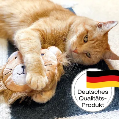 Rode kat speelt met leeuwen-pluche speelgoed. Tekst: Duits kwaliteitsproduct, Duitse vlag zichtbaar.