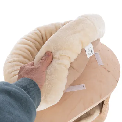 Hand hält ein abnehmbares, cremefarbenes Plüschkissen mit Etikett von 'Zooplus' über einer Holzoberfläche. Kissen zeigt Klettverschluss zur Befestigung.