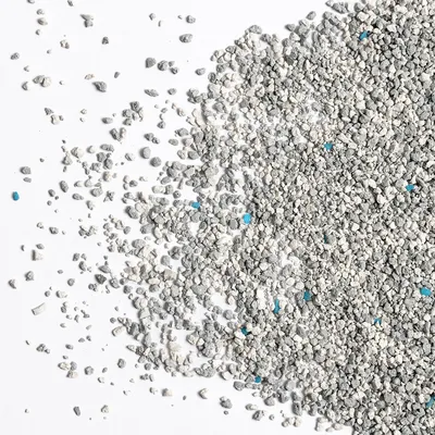 Graues und weißes Granulat mit vereinzelten blauen Körnern, lose auf weißem Hintergrund verteilt.