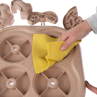 Hand cleaning a brown toy with a yellow cloth. Shows easy cleaning of the interactive pet toy with multiple compartments.