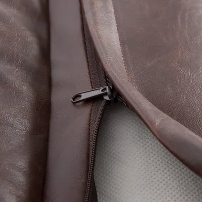 Zbliżenie na brązowy pokrowiec z ekoskóry z widocznym zamkiem błyskawicznym, pod którym znajduje się jasnoszara powierzchnia z drobną fakturą.