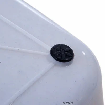 Valkoisen muovisen esineen kulma, jossa musta pyöreä liukuestetassu kukkakuviolla. Materiaali: muovi ja kumi.