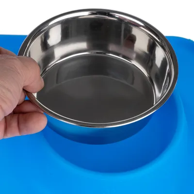Hand holding a stainless steel bowl over a blue non-slip mat with embossed paw patterns.