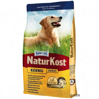 Happy Dog NaturKost Kernig Crunchy kutyatáp csomagolás, látható szöveg: Kein Soja!, Ohne Farb- & Konservierungsstoffe, német nyelvű összetevőlista, fűben fekvő kutya képe.