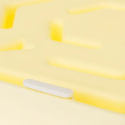 Nahaufnahme einer gelben Kunststoffoberfläche mit erhöhten Strukturen und einem weissen, rechteckigen Element.