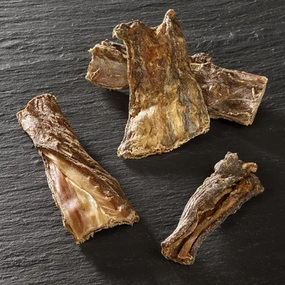Four pieces of dried, natural animal chew treats displayed on a dark surface.