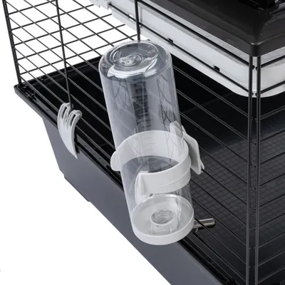 Trinkflasche aus transparentem Kunststoff mit weisser Halterung, befestigt an einem schwarzen Metallkäfig.