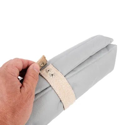Graue Stofftasche mit beige gemustertem Verschlussband und Druckknöpfen, von Hand geöffnet.