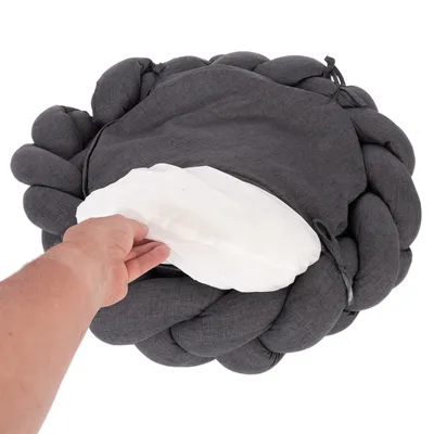 Hand visar en avtagbar vit kudde från en mörkgrå, flätad djursäng.