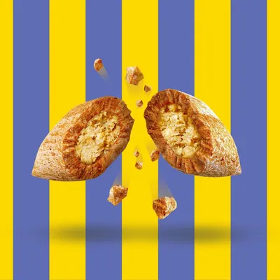 Croquette pour animal coupée en deux, montrant un intérieur fourré et des éclats autour, sur fond à rayures jaunes et bleues. Aucun texte ou marque visible.