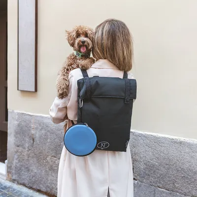 Donna con zaino nero e accessori blu, tiene un cane piccolo. Lo zaino mostra il logo 'NT'.