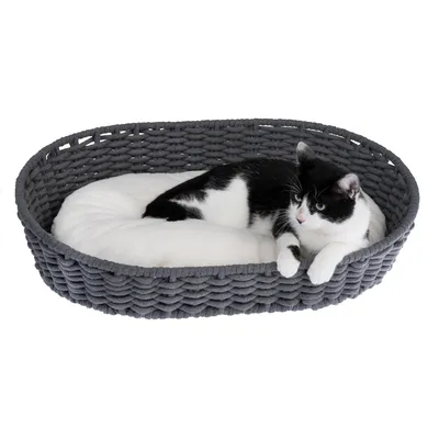 Gevlochten grijze mand met wit kussen, daarop ligt een zwart-witte kat.