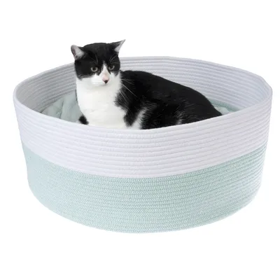 Schwarz-weisse Katze liegt in einem runden, zweifarbigen Katzenbett aus geflochtenem Stoff in Weiss und Mintgrün.