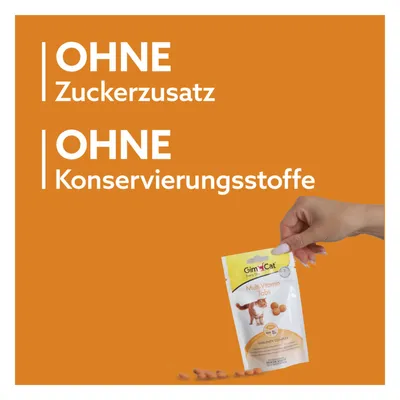 Texte en allemand : OHNE Zuckerzusatz, OHNE Konservierungsstoffe. Main tenant un sachet GimCat Multi-Vitamin Tabs pour chat, quelques comprimés visibles.