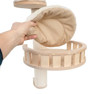 Hand showing removable, padded cushion made of beige fabric on a scratching post with wooden platform and sisal post.