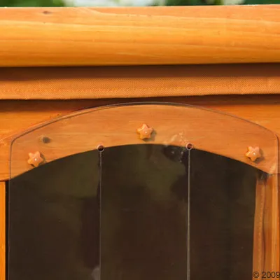 Close-up of a wooden pet house door with a transparent plastic flap and star-shaped fasteners at the top.
